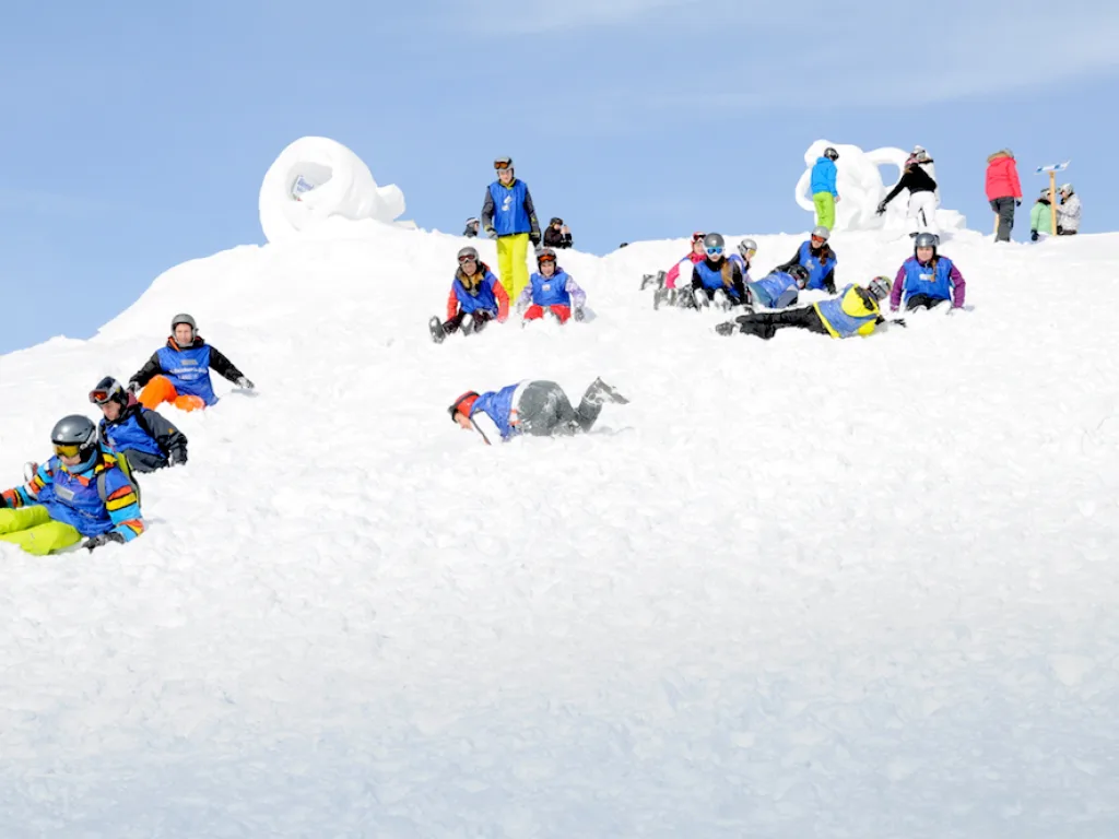 Jugendliche liegen und sitzen im Schnee am Hang.